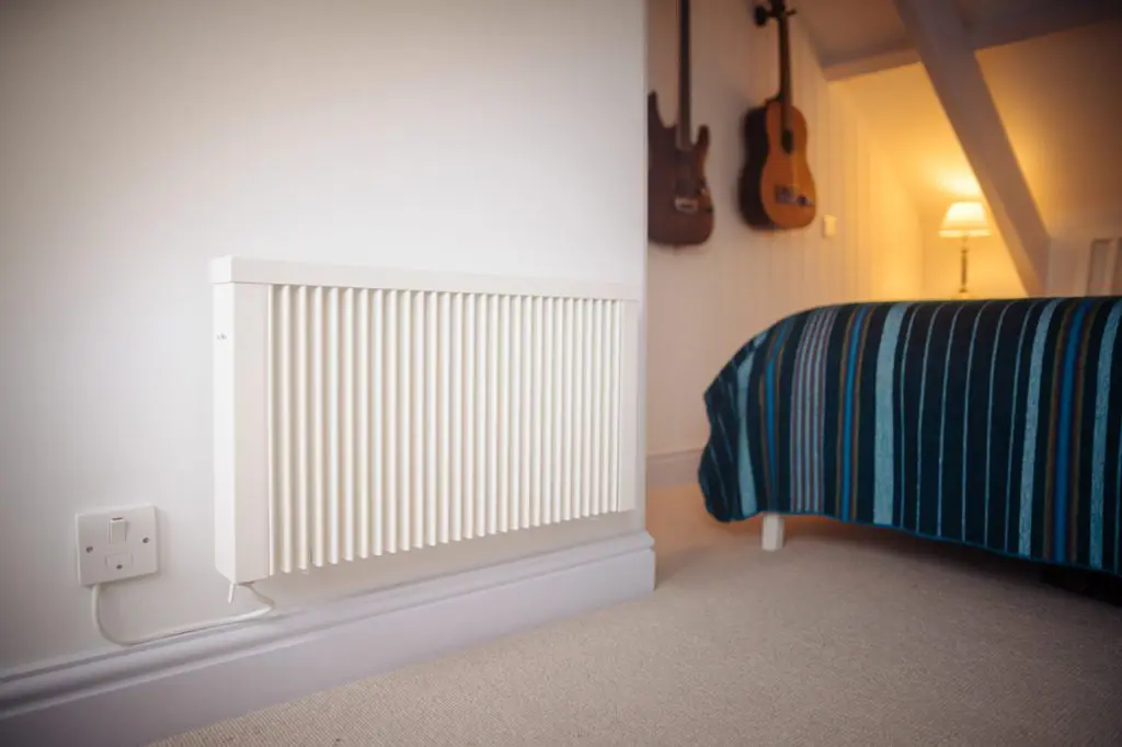 slimline efficient german electric radiator by south west heating solutions mounted on the wall in a bedroom, light side view
